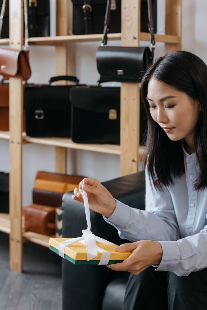 The Art of Drawing Readers In: Your attractive post title goes here Woman sitting indoors unwrapping a gift box surrounded by leather bags.